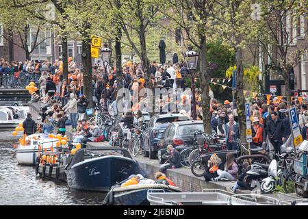 Menschenmassen, die auf den Straßen neben den Grachten von Amsterdam während der Feierlichkeiten zum Königstag gesehen werden. Der Königstag, bekannt als Koningsdag, ist ein orangefarbenes Fest zum Geburtstag des Königs, ein Nationalfeiertag voller Veranstaltungen im ganzen Land. Tausende von Einheimischen und Touristen besuchten Amsterdam, um an den Kanälen zu feiern und zu feiern, während sie orangefarbene Kleidung trugen und die Boote eine Parade in den Wasserkanälen machten. Stockfoto