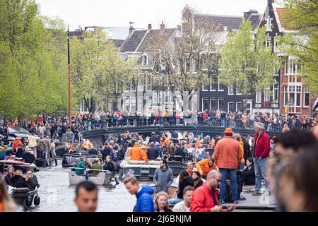 Menschen, die auf den Booten in den Grachten von Amsterdam während der Feier zum Königstag gesehen wurden. Der Königstag, bekannt als Koningsdag, ist ein orangefarbenes Fest zum Geburtstag des Königs, ein Nationalfeiertag voller Veranstaltungen im ganzen Land. Tausende von Einheimischen und Touristen besuchten Amsterdam, um an den Kanälen zu feiern und zu feiern, während sie orangefarbene Kleidung trugen und die Boote eine Parade in den Wasserkanälen machten. Stockfoto