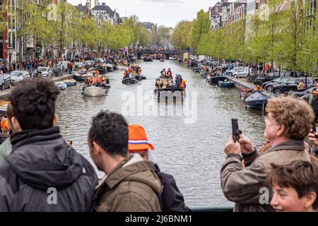 Menschen, die auf den Booten in den Grachten von Amsterdam während der Feier zum Königstag gesehen wurden. Der Königstag, bekannt als Koningsdag, ist ein orangefarbenes Fest zum Geburtstag des Königs, ein Nationalfeiertag voller Veranstaltungen im ganzen Land. Tausende von Einheimischen und Touristen besuchten Amsterdam, um an den Kanälen zu feiern und zu feiern, während sie orangefarbene Kleidung trugen und die Boote eine Parade in den Wasserkanälen machten. Stockfoto