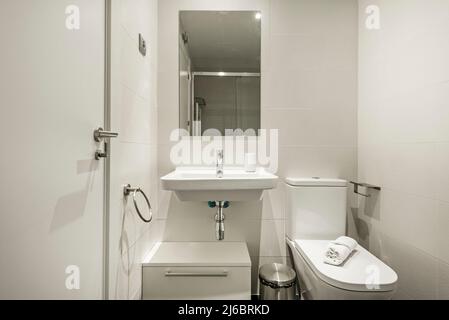 Badezimmer mit hängendem Waschbecken aus weißem Porzellan, großem rahmenlosen Spiegel und Edelstahlarmaturen Stockfoto