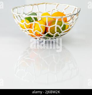 Silberner Metallkorb mit frischem Obst auf einer glänzenden weißen Theke Stockfoto