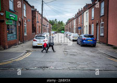 Mutter und Kind überqueren die Straße in der Dewsbury Road, einem benachteiligten Viertel in Wakefield, West Yorkshire. Stockfoto