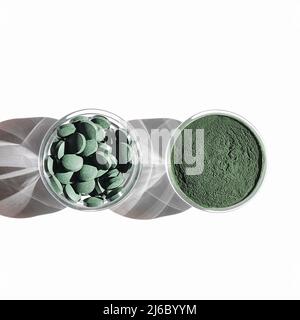 Natürliche Zusatzstoffe und Superfood. Grüne Spirulina Algenpulver und Pillen in Glas auf weißem Hintergrund. Gesundes Lifestyle-Konzept. Bio-Food-Quadrat Stockfoto