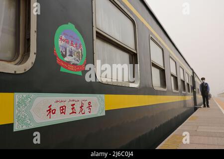 (220430) -- KASHGAR, 30. April 2022 (Xinhua) -- Auf dem Bahnsteig neben einem langsamen Zug, der nach Hotan in der Autonomen Region Xinjiang Uygur im Nordwesten Chinas fährt, wartet Ein Zugbegleiter auf Passagiere, 27. April 2022. Während Hochgeschwindigkeitszüge durch Bahnhöfe in vielen Teilen Chinas heranzoomen, bedienen die scheinbar veralteten, rumpelnden Hochgeschwindigkeitszüge weiterhin Bewohner abgelegener Gebiete mit stabilen Fahrkartenpreisen und Dienstleistungen. Obwohl China das weltweit am weitesten entwickelte Hochgeschwindigkeitsbahnnetz beherbergt, betreibt es immer noch regelmäßig 81 langsame Zugverbindungen. Die Züge 7556/7557 und 7558/7555, die zwischen Xinjiang verkehren Stockfoto