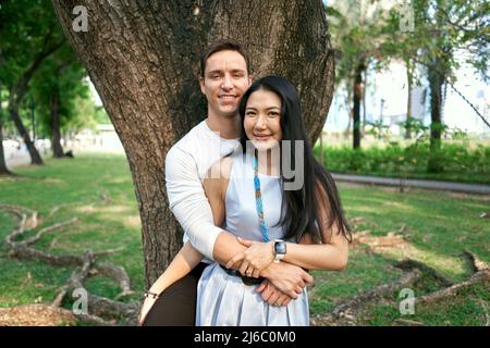 Nahaufnahme eines multiethnischen Paares, das sich in einem Baum anlehnt Stockfoto