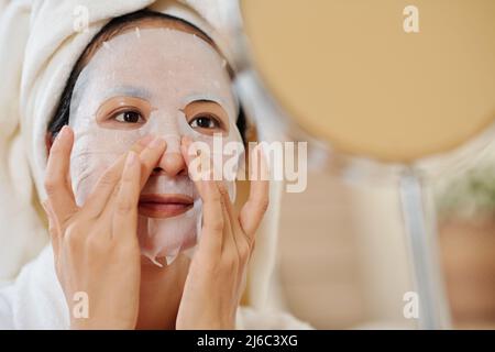 Junge Frau Anwendung Resurfacing Blatt Maske auf dem Gesicht vor Make-up zu tun Stockfoto