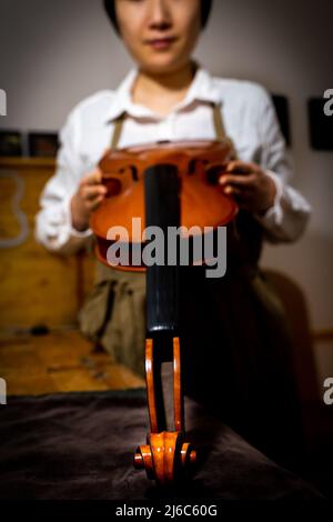 Die junge chinesische Geigenbauerin überprüft in der Werkstatt die Qualität ihrer Violine Stockfoto