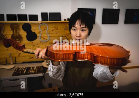 Die junge chinesische Geigenbauerin überprüft in der Werkstatt die Qualität ihrer Violine Stockfoto