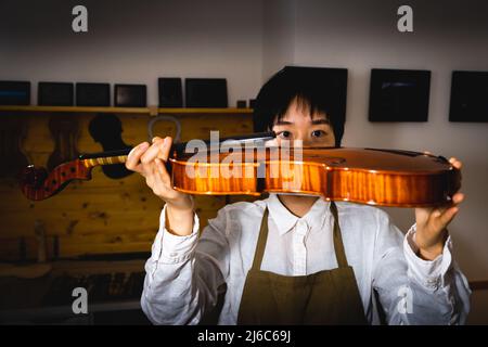 Die junge chinesische Geigenbauerin überprüft in der Werkstatt die Qualität ihrer Violine Stockfoto