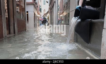 Person leert den Eimer mit Wasser aus dem überfluteten Laden in der Gasse von Venedig in Italien während der Flut Stockfoto