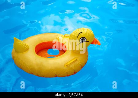 Gelbes aufblasbares Duckling-Spielzeug aus Kunststoff, das im blauen Pool mit Wasser schwimmt Stockfoto