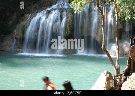 Wasserfall auf einem sauberen smaragdgrünen Fluss bedeckt eine kleine Höhle, an einem der Kaskaden der Erawan Falls in Thailand Stockfoto