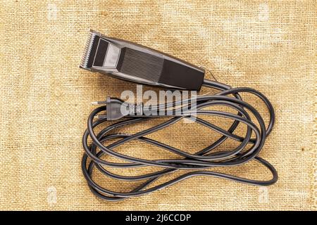 Ein elektrischer Haarschneider auf Jute-Stoff, Makro, Draufsicht. Stockfoto