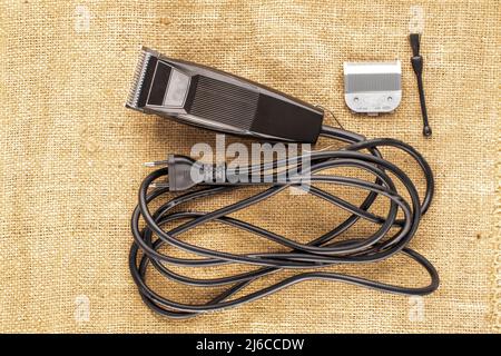 Ein elektrischer Haarschneider auf Jute-Stoff, Makro, Draufsicht. Stockfoto