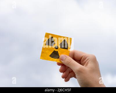 Eine Frau mit einem Strahlungswarnschild in der Hand vor einem bewölkten Himmel. Nahaufnahme. Stockfoto