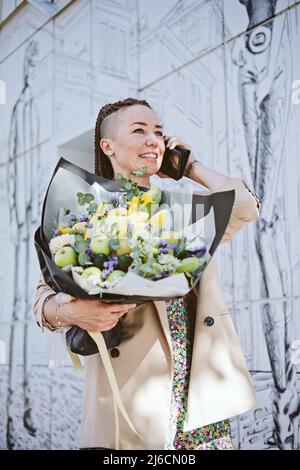 Lieferung von Blumen. Junge moderne Hipster Frau mit Handy erhalten schöne Blumen Blumenstrauß von Lieferung im Freien Stockfoto