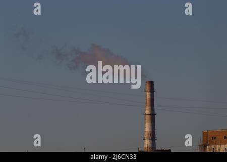 Rohre einer alten Fabrik werfen Wolken aus giftigem weißem Rauch in den Himmel, die die Atmosphäre verschmutzen. Städtischer Smog durch Rauch aus Kesselhäusern. Weiße s Stockfoto