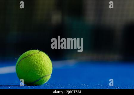 Padel-Tennisball auf einem blauen Platz, wobei das Netz im Hintergrund nicht fokussiert ist. Schlägersportkonzept. Stockfoto