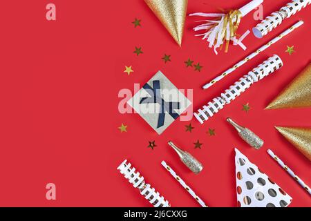 Goldene Partyhüte, kleine Champagnerflaschen, Sternkonfetti und Geschenk auf rotem Hintergrund Stockfoto