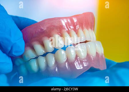 Zahnprothese in den Händen des Arztes Nahaufnahme. Zahnarzt hält keramische Zahnbrücke. Vorderansicht der kompletten Prothese. Zahnmedizin konzeptionelle pho Stockfoto
