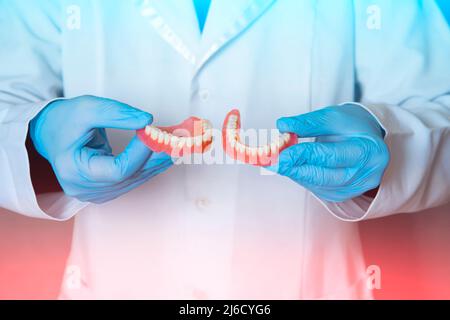 Zahnprothese in den Händen des Arztes Nahaufnahme. Zahnarzt hält keramische Zahnbrücke. Vorderansicht der kompletten Prothese. Zahnmedizin konzeptionelle pho Stockfoto