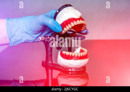 Zahnprothese in den Händen des Arztes Nahaufnahme. Zahnarzt hält keramische Zahnbrücke. Vorderansicht der kompletten Prothese. Zahnmedizin konzeptionelle pho Stockfoto