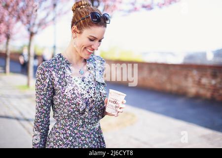 Glückliche junge Frau lächelt mit einer Tasse Kaffee im Freien Stockfoto