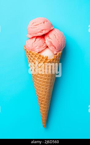 Eis auf blauem Hintergrund. Drei Kugeln Beereneis in einem Waffelbecher auf blauem Hintergrund. Stockfoto