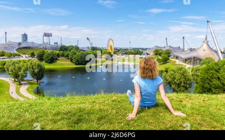 Mädchen im Olympiapark, München, Deutschland. Junge Frau sitzt im Münchner Vergnügungsviertel auf Gras, im Sommer ruht die Person. Dieser Ort ist touristisch atractio Stockfoto