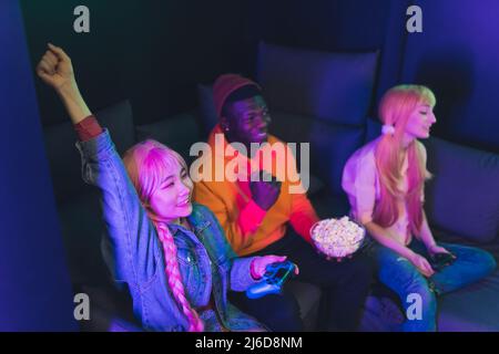 Freunde verbringen gerne Zeit zusammen, spielen Videospiele mit dem Spielpad, essen Popcorn, während sie auf einer Couch sitzen. Hochwertige Fotos Stockfoto