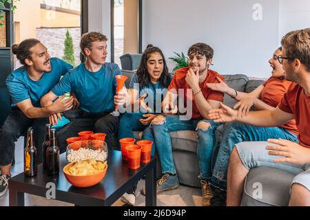 Glückliche Freunde, die Sportereignisse im Fernsehen verfolgen, einer von ihnen wechselt den Kanal und macht die anderen wütend. Stockfoto