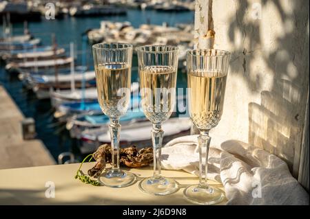 Drei Gläser französischer Champagner Sekt und Blick auf bunte Fischerboote im alten Hafen von Cassis, Provence, Frankreich, Sommerfest in PR Stockfoto