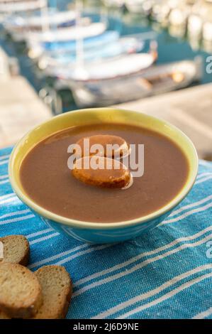 Hausgemachte leckere Fischsuppe mit Croutons, serviert mit Blick auf bunte Fischerboote im Hafen von Cassis, Privence, Frankreich. Provenzalische Küche. Stockfoto