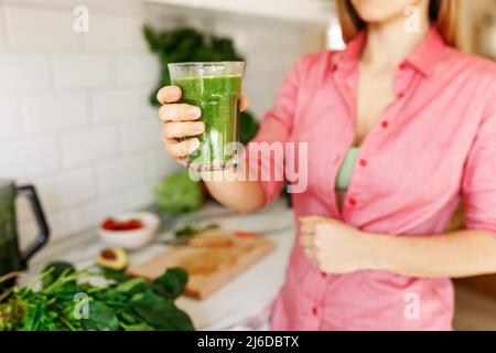 Green Smoothie - gesunde Ernährung Konzept. Gesichtslose Frau hält Smoothie Shake gegen Küche Haus Innenraum, konzentrieren sich auf Hände und Glas Stockfoto