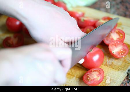 Cook schneidet Tomaten auf Holzbrett Nahaufnahme Stockfoto