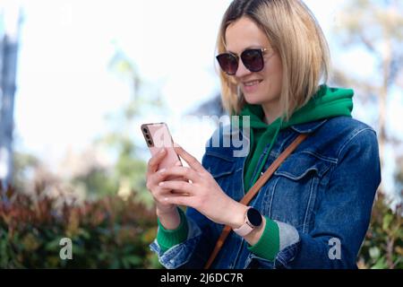 Lächelnde Frau schaut auf das Telefon auf der Straße Stockfoto