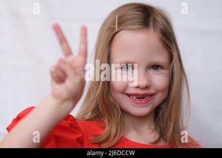 Lächelndes kleines Mädchen ohne Vorderzähne Geste zwei Finger nach oben Stockfoto