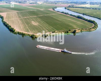 Kleines Schleppboot schiebt Barge entlang ruhigem Wasser vorbei an Feldern Stockfoto