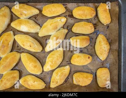 Legen Sie die frisch gebackenen Pasteten mit der Füllung auf ein mit Backpapier bedecktes Backblech. Köstliche frische hausgemachte Backwaren aus dem Ofen. Draufsicht. Stockfoto