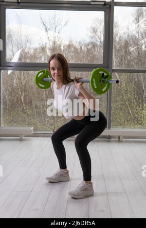 Ihre Hände lächelt Mädchen in Langhantel die A mit Langhantel starke weibliche Frau, für schwer gesund in der Kraft aus dem Training eine, halten Kreuz. Sport Stockfoto