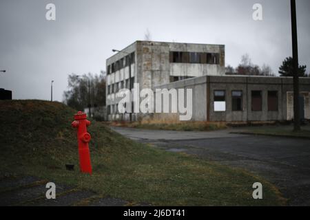 Leuchtender roter Hydrant, der sich vor zerstörten Betongebäuden absticht. Stockfoto