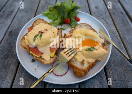 Croissant-Sandwich mit pochiertem Ei, Rettich und Lachs auf dem Teller im Café, Nahaufnahme Stockfoto