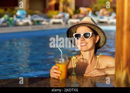 Lächelnde Frau, die einen Cocktail an der Poolbar trinkt Stockfoto