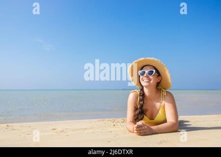 Lächelnde Frau mit Weihnachtshut und Sonnenbrille am Sandstrand Stockfoto
