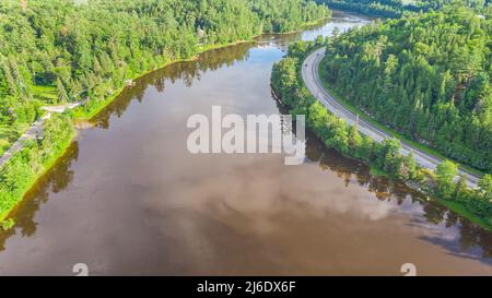 Luftaufnahme des Gatineau Flusses in der Nähe des Dorfes Wakefield, Kanada. Wolken, die sich im Flusswasser spiegeln, schlängelt sich eine Straße mit Autos entlang des Kurses Stockfoto