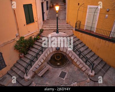 LUFTAUFNAHME von einem 6-Meter-Mast. Charmante Treppe mit einem kleinen Brunnen in der Altstadt von Villefranche-sur-Mer. Französische Riviera, Frankreich. Stockfoto