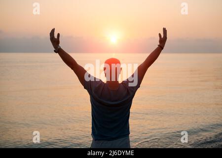 Silhouette Mann mit seinen Händen angehoben bei Sonnenuntergang am Strand Arme nach Seiten in Richtung der Sonne, Konzept für Religion, Anbetung, Gebet und Lob und Erfolg im Leben, Frieden und Ruhe in der Natur Stockfoto