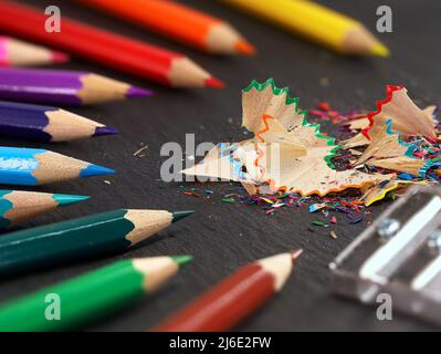 Geschärfte Buntstifte, Buntstifte und Spitzer mit Bleistiftspalten auf schwarzem Schieferhintergrund, Nahaufnahme Stockfoto