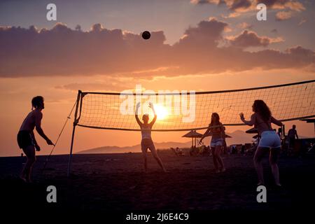 Eine Gruppe junger Freunde, die am Strand bei Sonnenuntergang Beach Volley spielen. Stockfoto