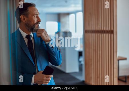 Ein erwachsener bärtiger Geschäftsmann schaut im Büro nachdenklich weg Stockfoto